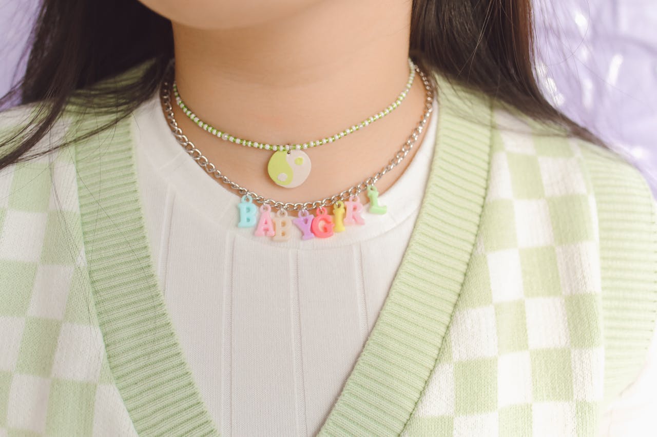 Close-up of colorful layered necklaces worn over a green checkered vest, showcasing trendy fashion accessories.